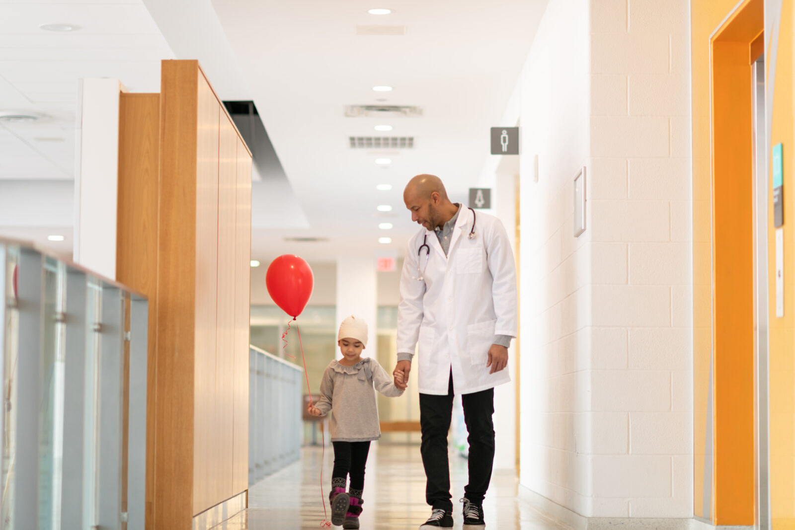 Child with balloon holds doctor's hand in hospital corridor