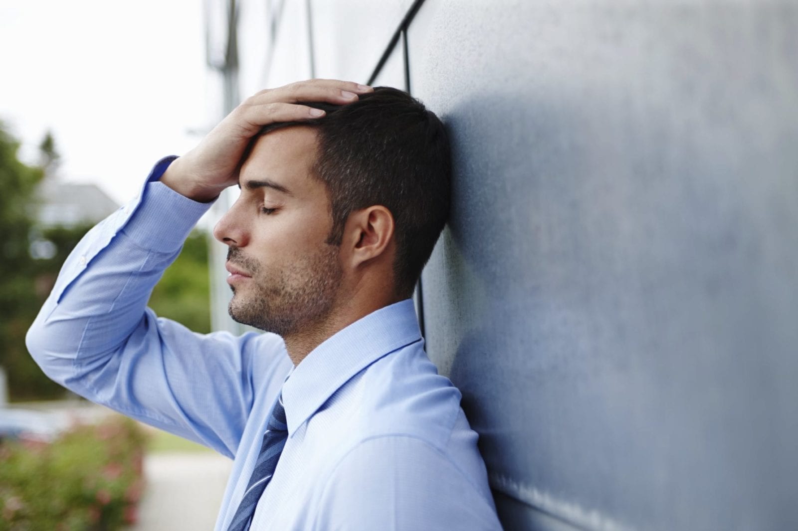 A stressed young businessman standing outdoors with his head in his hands